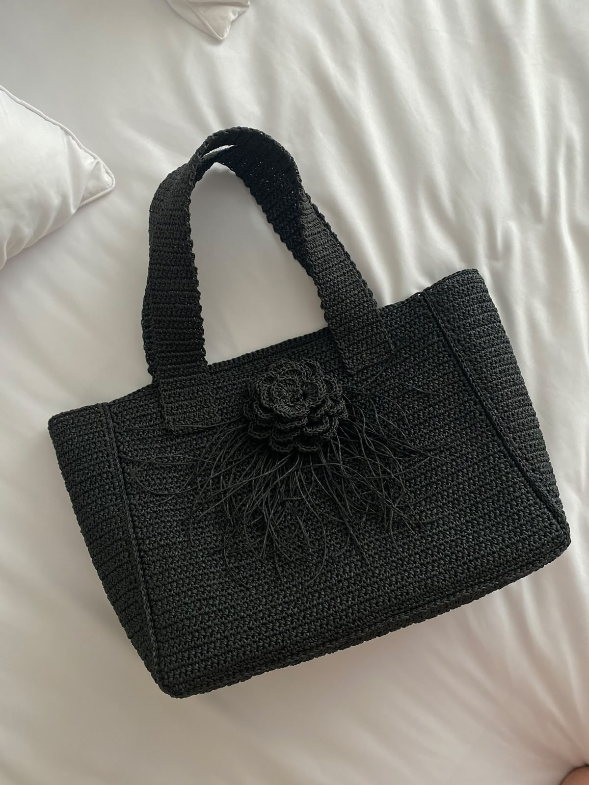 Black handcrafted TarNina crochet tote bag adorned with a handmade floral rose ornament, resting on white linen