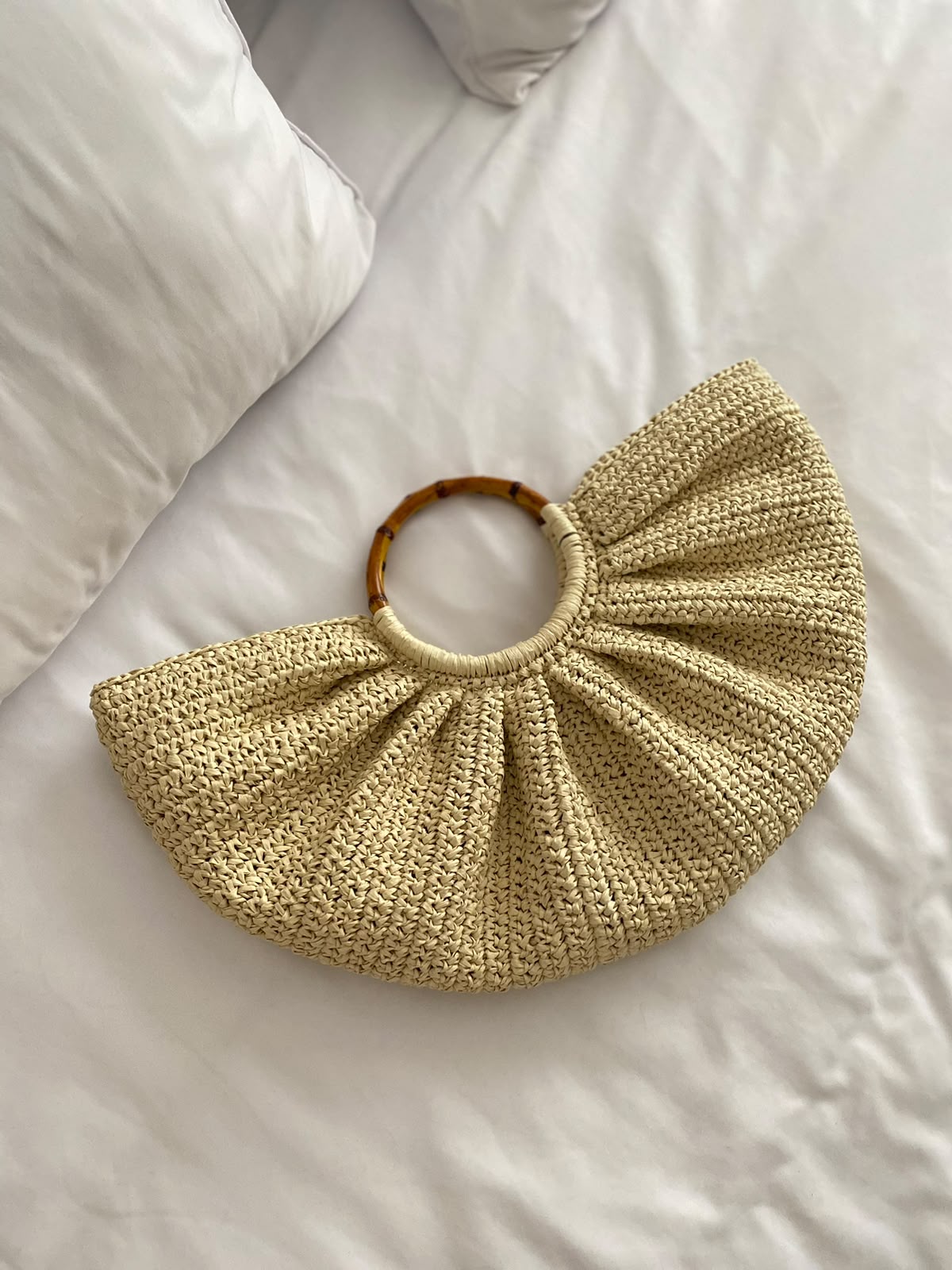 Natural-tone TarNina woven fan-shaped bag with bamboo circular handles, resting on white linen